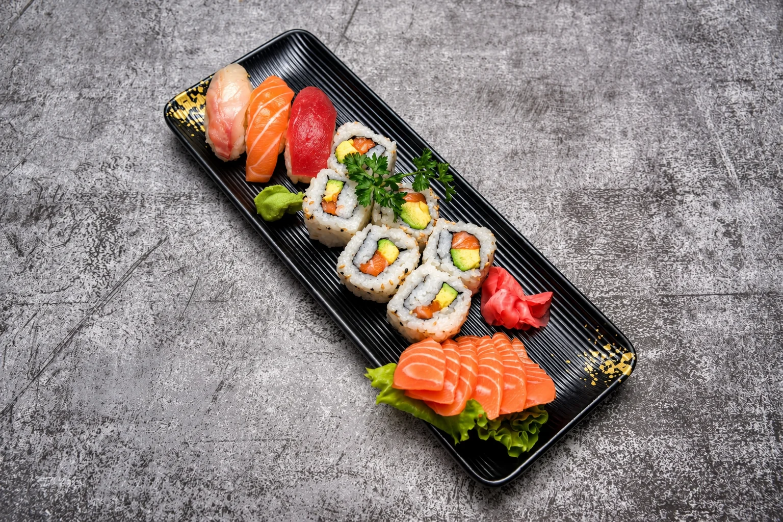 Nigiri, california et sashimi saumon sur une assiette noire rectangulaire, fond de béton gris.